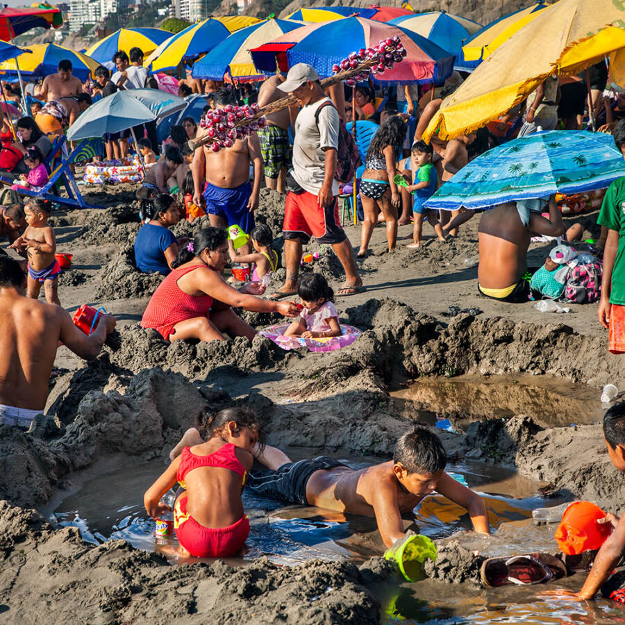 Una multitud de gente disfrutando un día en la playa Aguadulce. Sombrillas coloridas, azules y amarillas. Adultos y niños jugan en la arena.