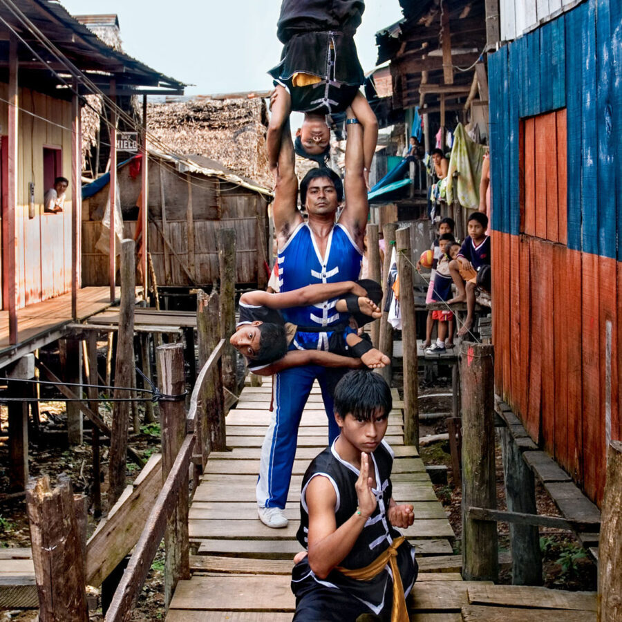 Familia de acróbatas realizando una torre humana de tres niveles sobre un puente de madera en el barrio de Belén, Iquitos.