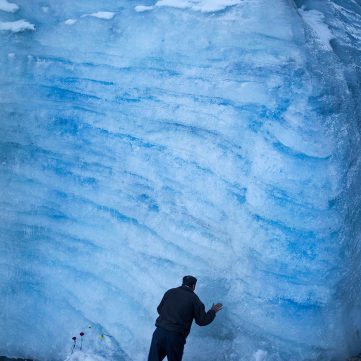 Hombre de espaldas reza tocando una inmensa pared de hielo azul en la peregrinación del Señor de Qoyllur Riti.